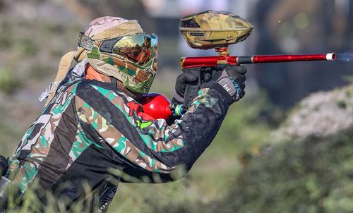 Woodsball player firing from natural brush cover in camo